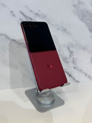 A Motorola smartphone with a split black and deep red back panel, displayed on a silver metal stand against a white marble-patterned background.