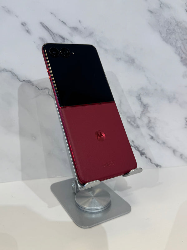 A Motorola smartphone with a split black and deep red back panel, displayed on a silver metal stand against a white marble-patterned background.