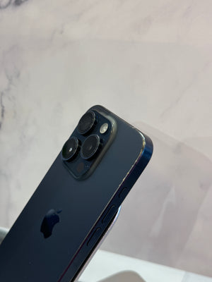 Close-up of the rear upper corner of a dark blue Apple iPhone showing the camera module and part of the Apple logo, set against a light marble-patterned background.