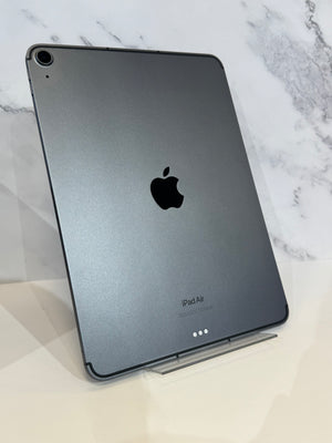 A dark gray Apple iPad Air standing upright on a clear display stand against a white marble-patterned background.