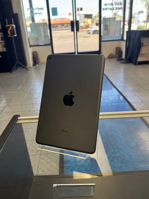 A silver Apple iPad shown from the back, resting on a clear display stand inside a retail store.