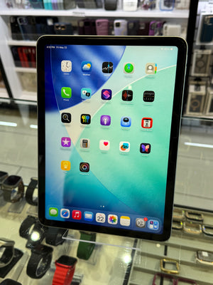 Tablet with app icons displayed on a glass surface with electronic devices in the background