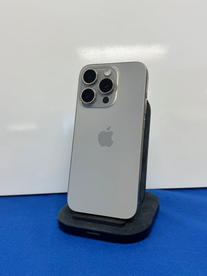 A silver Apple iPhone Pro standing upright on a black charging dock against a white background with a blue surface below.