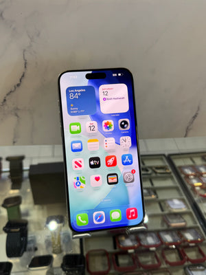 A black iPhone with its screen on, displaying the home screen, resting on a display stand in a watch and phone store.
