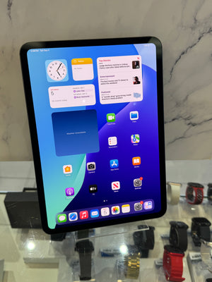 A black tablet device displaying a colorful home screen, standing upright on a glass display counter with other watches and accessories in the background.