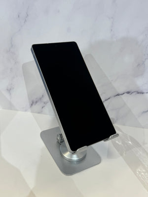 A black smartphone displayed at an angle on a silver metal stand, set against a white marble-patterned background.