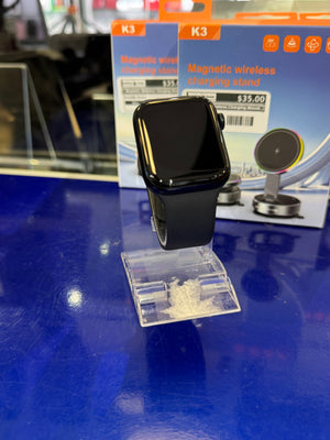 Smartwatch on a clear stand with K3 magnetic wireless charging stand packaging in the background.