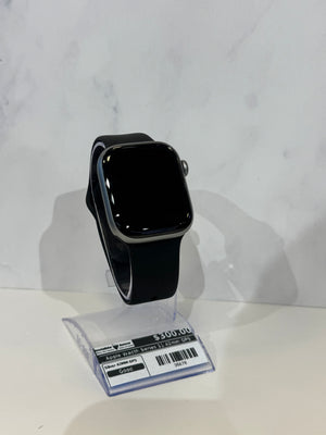 A black smartwatch with a rectangular face and black band, displayed on a clear plastic stand with a price tag. The watch has a silver-toned metal case.