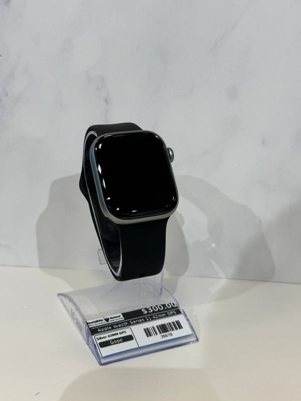 A black smartwatch with a rectangular face and black band, displayed on a clear plastic stand with a price tag. The watch has a silver-toned metal case.