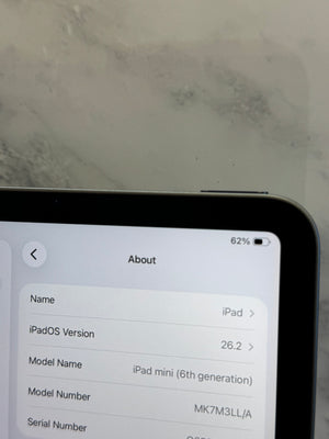 A close-up of a tablet screen showing the iPad About page with iPadOS Version 26.2 and Model Name iPad mini (6th generation), set against a light marble-patterned background.