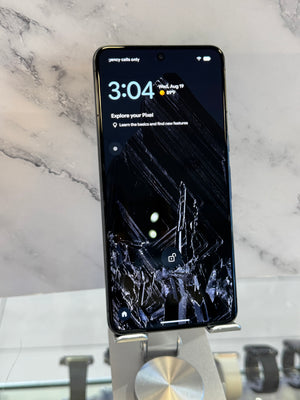 A black smartphone is displayed upright on a metal stand against a light marble-patterned background.