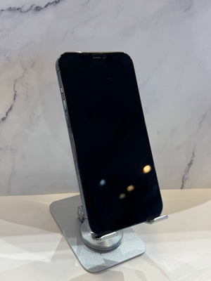 A black smartphone with a dark screen stands upright on a silver metal display stand against a light marble-patterned background.