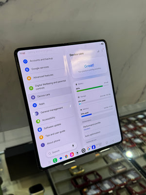 A foldable smartphone displayed at an angle on a stand, showing its software interface with a light gray background and a blurred retail counter below.