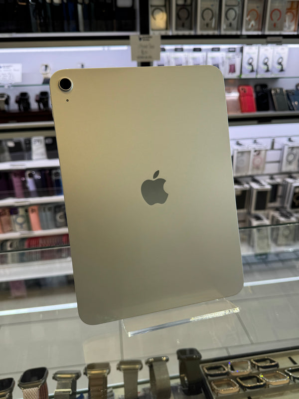 An Apple iPad shown from the back, resting on a clear display stand inside a retail store with shelves of other electronics in the blurred background.