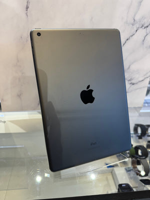 A silver Apple iPad shown from the back, resting on a glass display counter against a marble-patterned wall.