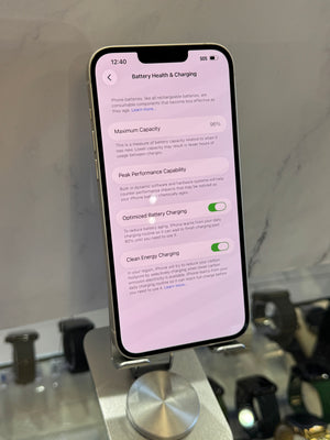 A smartphone on a display stand showing the Battery Health & Charging settings screen, photographed in a retail or showroom environment with blurred devices in the background.