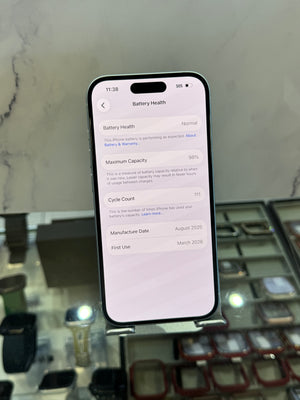 A black smartphone displaying battery health details on its screen, held upright in a retail or display setting with a marble-patterned background.