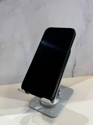A black smartphone displayed upright on a silver metal stand against a light marble-patterned background.