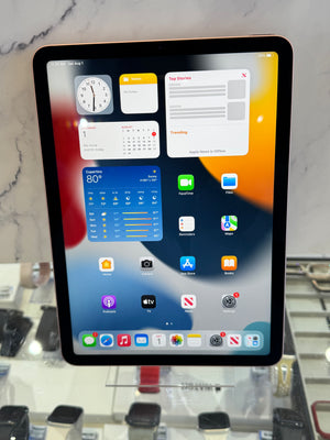 An iPad with a black bezel displaying its home screen, resting on a white marble surface with a blurred retail store background.