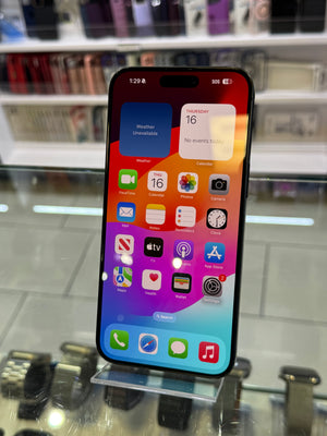 A black iPhone with a colorful home screen displayed on a clear stand in a retail store setting.