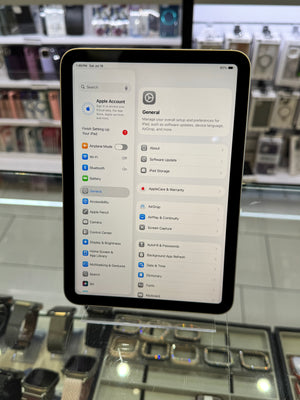 A tablet device displaying the Apple Settings app, photographed in a retail store environment with display cases and electronics in the blurred background.