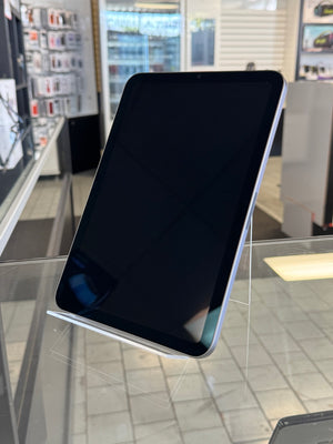 A black tablet device with rounded corners, displayed at an angle on a clear acrylic stand inside a retail store.