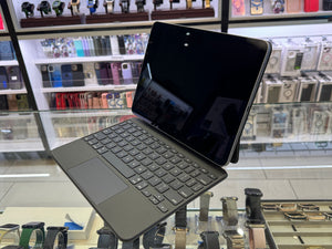 A dark gray Microsoft Surface Pro tablet with a matching keyboard cover and kickstand, displayed on a glass counter inside a retail store.