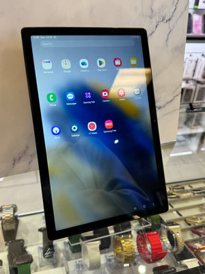 A black tablet with a lit home screen displaying various app icons, resting on a light marble countertop in a retail store environment.