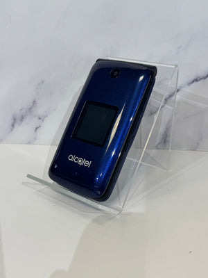 A blue Alcatel flip phone with a glossy finish, displayed on a clear acrylic stand against a white marble-patterned background.
