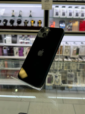 A black Apple iPhone 12 Pro shown from the back, resting on a clear acrylic display stand inside a retail store.