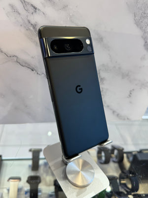 A Google Pixel smartphone shown from the back, resting on a small metallic display stand against a light marble-patterned background.