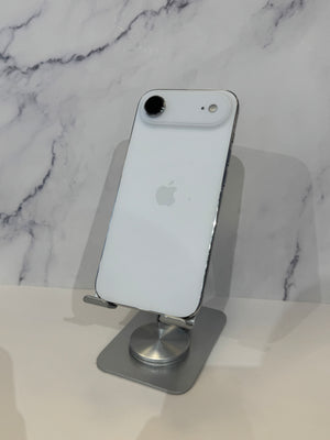 A white Apple iPhone with a silver bumper is shown from the back, resting on a silver metal stand against a white marble-patterned background.