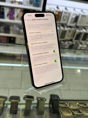 A black smartphone on a glass display case in a retail store. The screen is on and displaying battery-related settings in English.