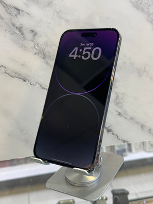 A black smartphone with a purple lock screen wallpaper is mounted on a silver magnetic display stand on a white marble surface.
