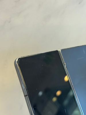 Close-up of a black smartphone screen and a dark metallic frame, resting on a light marble surface.