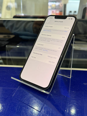 A black smartphone shown at an angle on a clear acrylic display stand, with its screen turned on and displaying battery-related settings. The phone is photographed in a retail or showroom environment with a blue surface and blurred background.