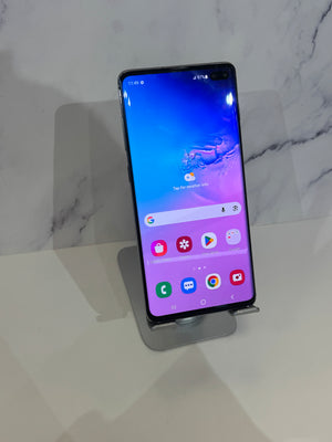 A Samsung Galaxy smartphone with a black bezel and a colorful blue-to-purple home screen, displayed on a small metallic stand against a white marble-patterned background.