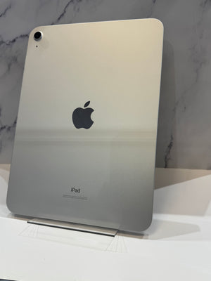 An Apple iPad with a metallic silver back panel, standing upright on a clear display stand against a gray marble-patterned background.
