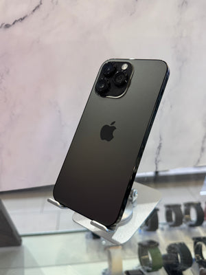 A black Apple iPhone 12 Pro shown from the back, resting on a silver metal display stand in front of a light marble-patterned wall.