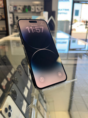 A black iPhone with a dark blue and pink gradient lock screen wallpaper, displayed on a clear glass stand inside a retail store.