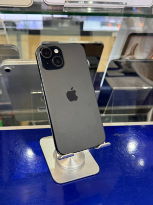 A dark gray Apple iPhone 12 Pro shown from the back, resting on a white stand in a retail display with a blue counter in the background.