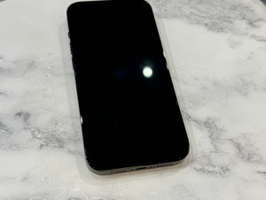 A black smartphone with a blank screen lies on a white marble surface with gray veining.