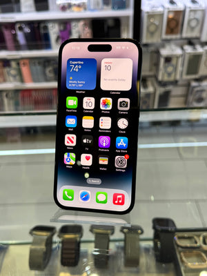 A black smartphone with a large front-facing display showing the home screen, photographed in a retail or display environment with blurred devices in the background.