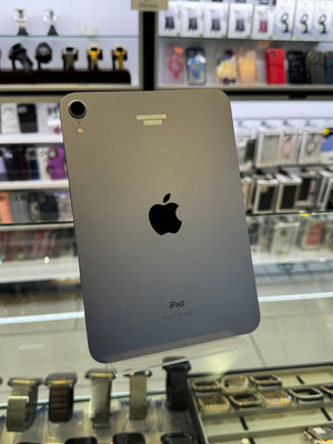A silver Apple iPad shown from the back, featuring the iconic black Apple logo and 'iPad' text, photographed inside a retail store display with blurred accessories in the background.