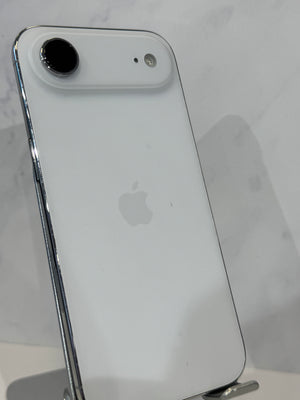 A white Apple iPhone with a single rear camera, shown from the back on a display stand against a light marble-patterned background.