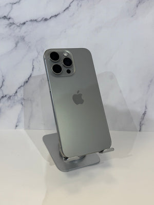 A silver Apple iPhone 12 Pro shown from the back, resting on a clear phone stand against a white marble-patterned background.