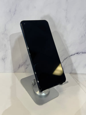 A black smartphone with a blank screen, resting on a silver metal stand against a white marble-patterned background.