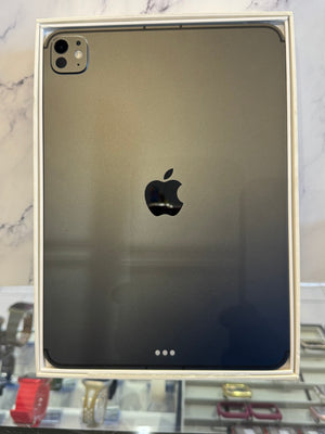 A black Apple iPad with a glossy back, presented inside its original white cardboard packaging box. The Apple logo is clearly visible in the center of the device.