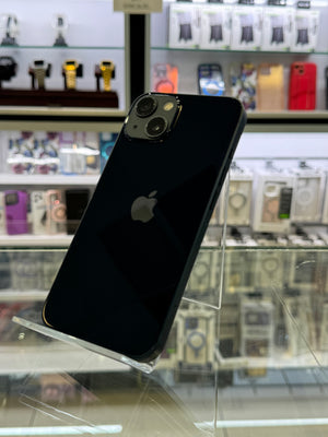 A black Apple iPhone with a glossy finish is displayed on a clear acrylic stand inside a retail store. The Apple logo is visible on the back of the phone, and blurred product displays are in the background.
