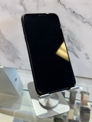A black smartphone with a large front-facing display, shown upright on a silver metal stand in a retail or showroom setting with a marble-patterned background.